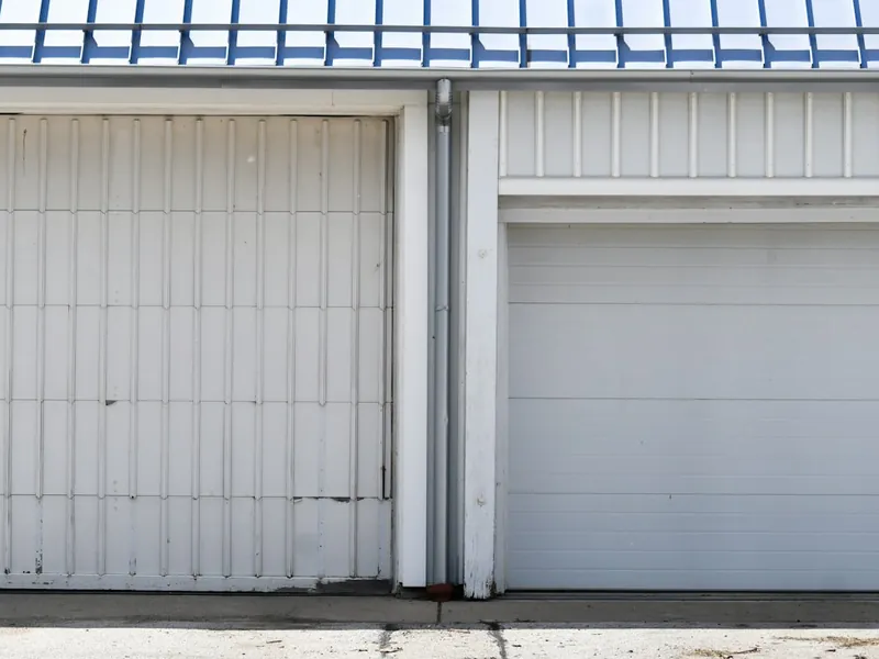 Two white garage doors side by side, one needing off-track repair